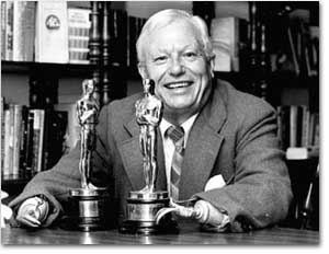 Harold Russell sitting and smiling while wearing a suit with two trophies in front of him