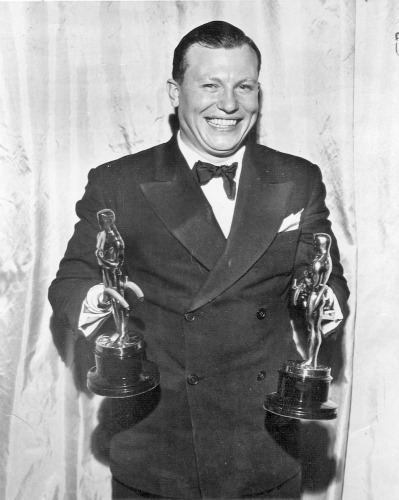 Harold Russell smiling and holding two trophies while wearing a suit