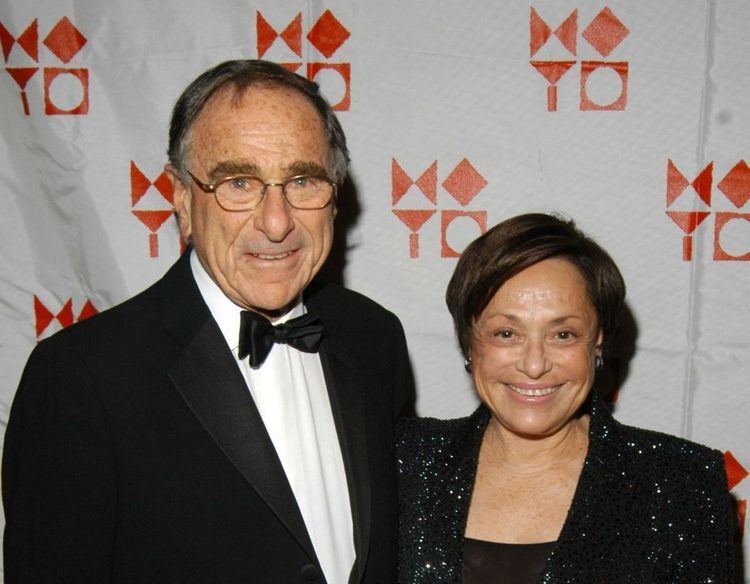 Harry B Macklowe smiling with Linda Macklowe while wearing eyeglasses, black coat, white long sleeves, and bow tie