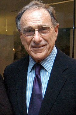 Harry B. Macklowe smiling while wearing eyeglasses, black coat, blue striped long sleeves, and necktie