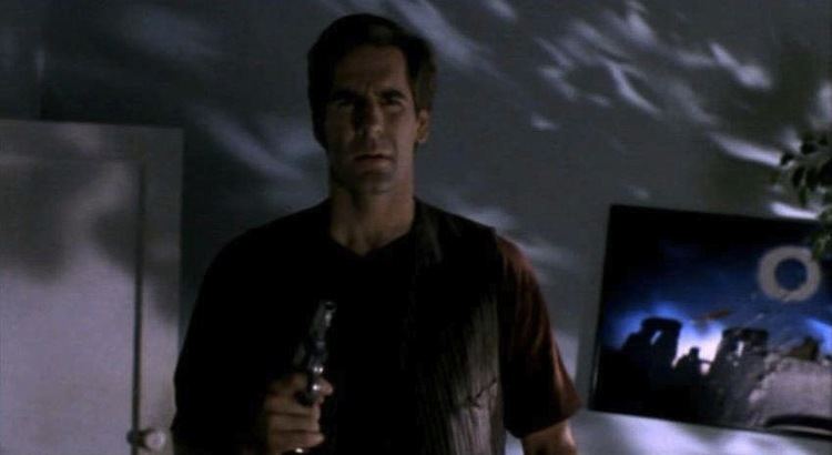 Scott Bakula as Harry D'Amour with a serious face while holding a gun in a movie scene from Lord of Illusions, a 1995 neo-noir supernatural horror film.