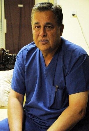 Hasnat Khan sitting on the bed wearing a surgical uniform