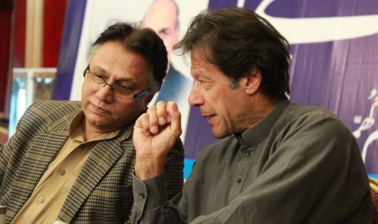Hassan Nisar wearing eyeglasses, a checkered coat, and a brown polo shirt while talking with a man wearing long sleeves.