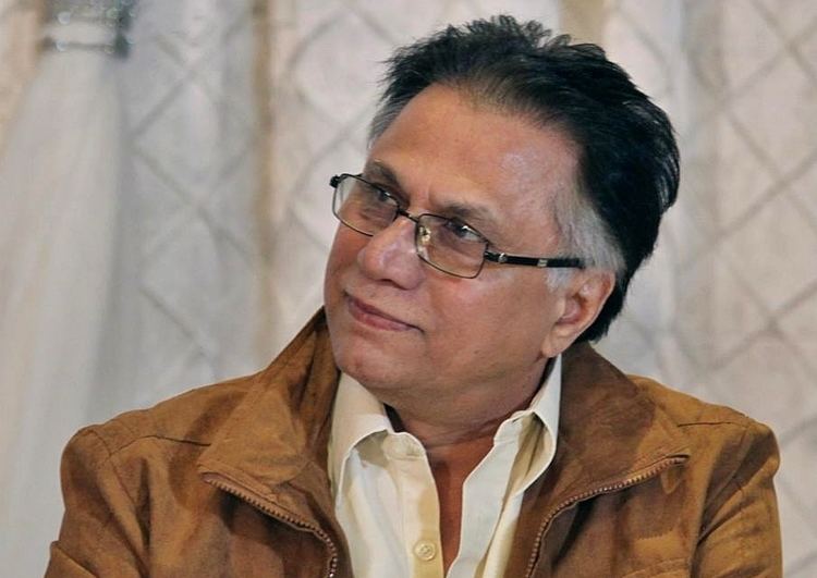 Hassan Nisar smiling and wearing eyeglasses and a brown jacket.