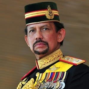 Hassanal Bolkiah with a serious face while looking at something, with a beard and mustache, wearing a multi-colored forage cap with a badge on it, and identification badges in a multi-colored service uniform