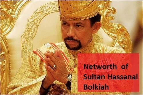 Hassanal Bolkiah with a serious face while looking at something and holding his own hands together while sitting on a throne, wearing a yellow headdress, a ring, a watch, and a yellow robe.
