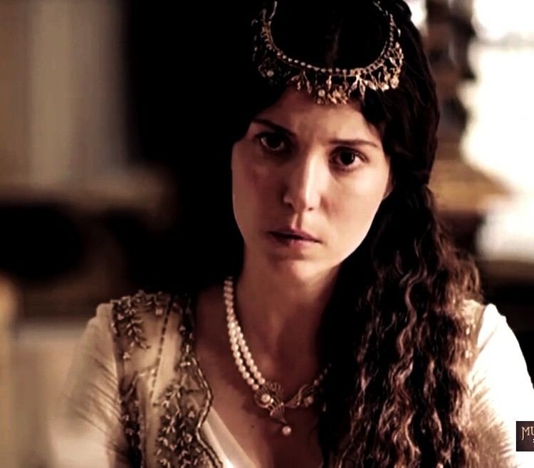 Hatice Sultan with curly hair while wearing head jewelry, pearl necklace, and cream and brown blouse
