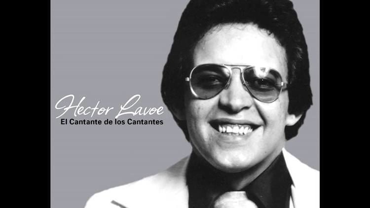 Hector Lavoe smiling and wearing a black shirt and white suit with eyeglasses and necktie in a black and white poster