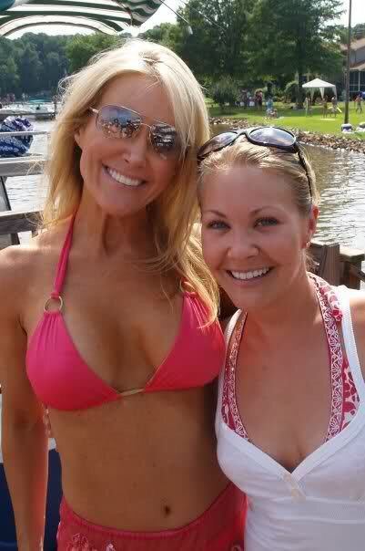 Heather Childers and her friend are smiling. Both with blonde hair and wearing sunglasses. Heather is wearing a pink two-piece swimsuit while her friend is wearing a white sleeveless top over a red and white swimsuit with visible cleavage.