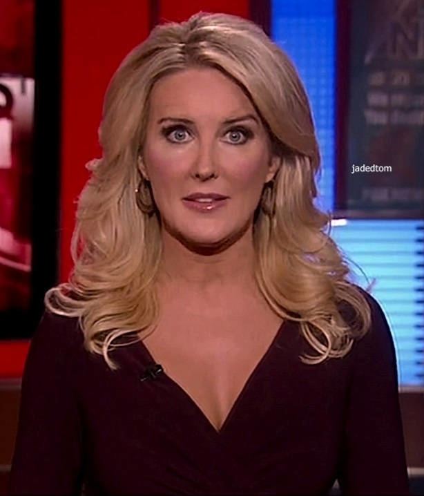 Heather Childers with a surprised face, wavy blonde hair, wearing earrings, and a wireless microphone on her maroon dress with a deep V-cut.