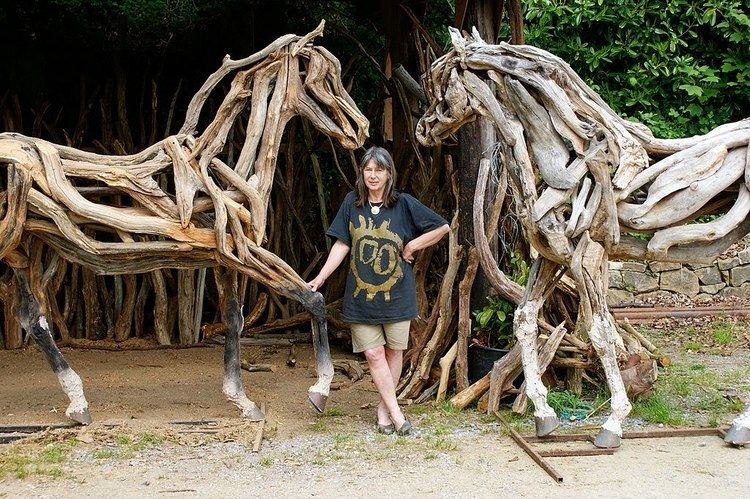 Sculptor Heather Jansch flanked by two of her driftwood horses, "Atlantis" on her right and "The Eden Horse" on her left.