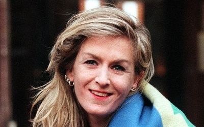 Heather McCartney smiling with blonde hair while wearing earrings and a blue, yellow, and green jacket