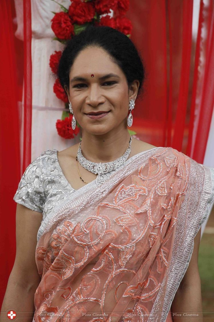 Heeba Shah standing and smiling while wearing silver earrings, necklace, and a dress