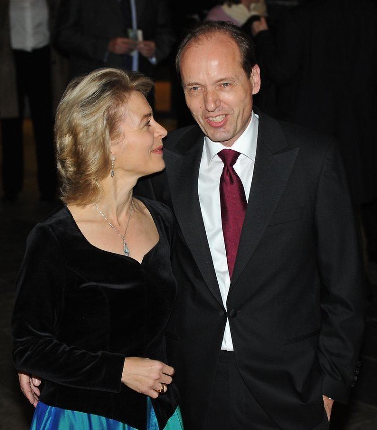 Heiko von der Leyen smiling while wearing a formal suit while Ursula von der Leyen wearing black long sleeves and a blue skirt