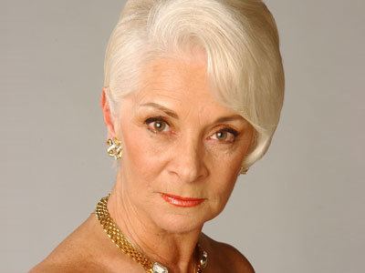Helen Richey with a fierce look, white hair, wearing gold earrings and a gold necklace.