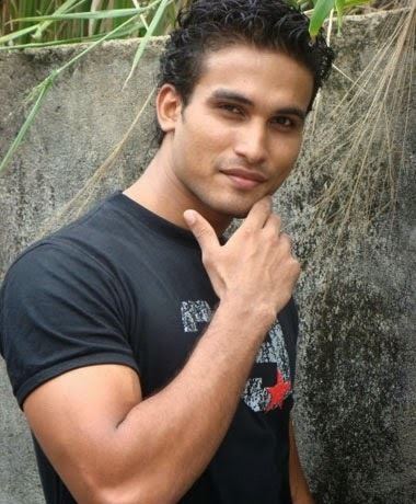 Hemal Ranasinghe with a tight-lipped smile while hand on his chin and wearing a black printed t-shirt