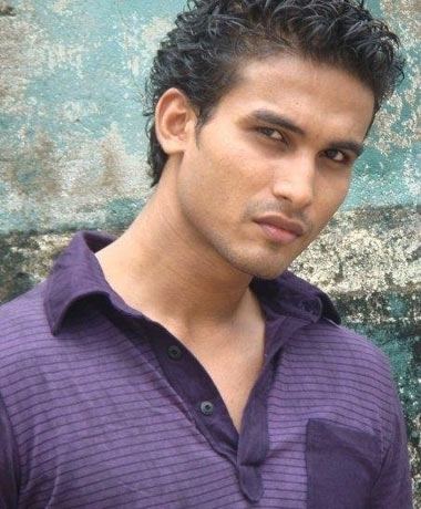 Hemal Ranasinghe with a serious face while wearing a violet striped polo shirt