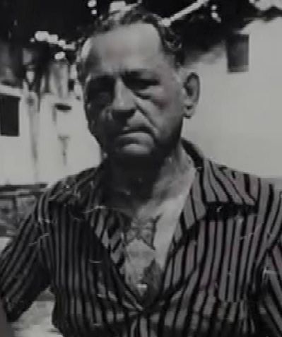 Henri Charrière with a serious face and wearing a striped polo shirt.