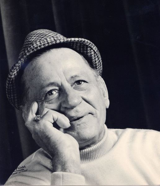Henri Charrière smiling and wearing a checkered hat and a ring.