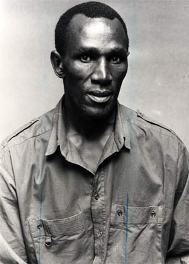 Henry Cele with a tight-lipped smile while wearing a long-sleeved