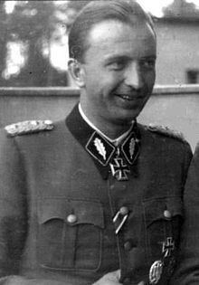 Hermann Fegelein smiling while wearing gray and black long sleeves with badge