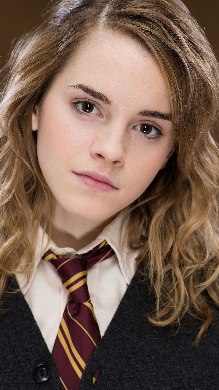 Emma Watson as Hermione Granger slightly smiling with a blonde curly hair, in the J.K. Rowling novel series, Harry Potter, wearing a red and yellow checkered necktie, white inner polo under a black coat