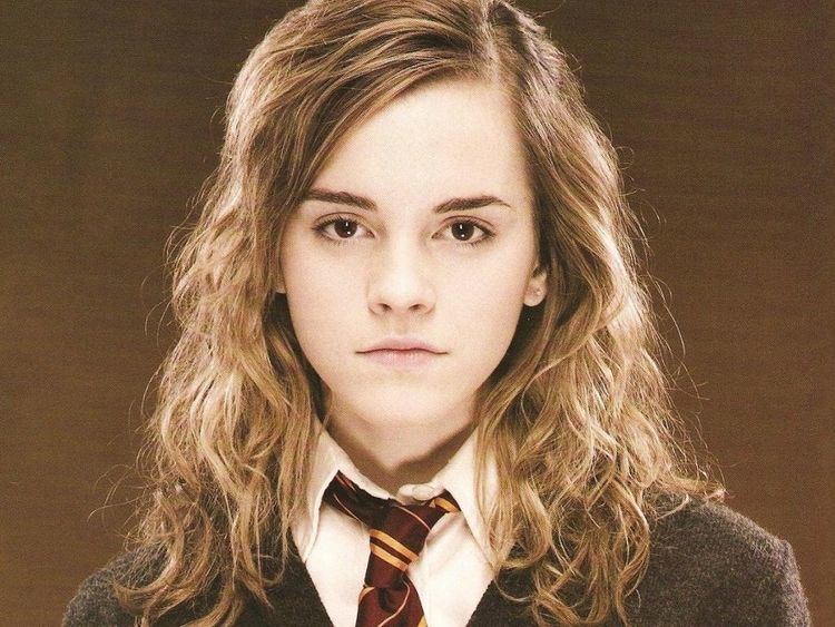 Emma Watson as Hermione Granger with a serious face and with a blonde curly hair, in the J.K. Rowling novel series, Harry Potter, wearing a red and yellow checkered necktie, a white polo under a black coat