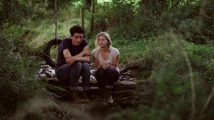 Josh O'Connor sitting next to Hannah Arterton in the forest in a scene from the 2014 romantic drama film, Hide and Seek