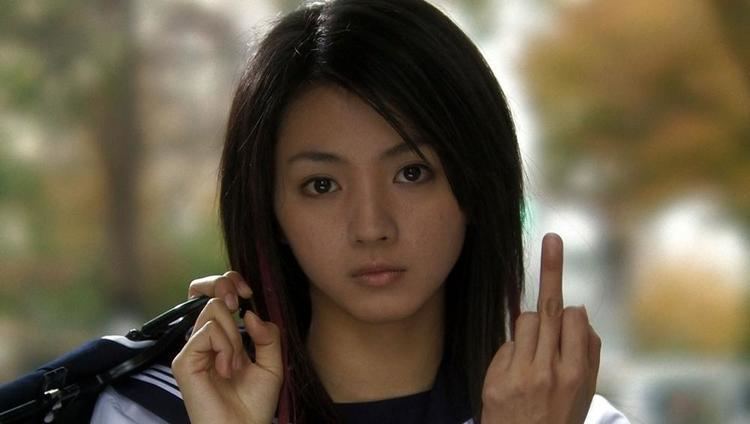 Hikari Mitsushima is serious and has black hair with red highlights, left hand, middle finger up, right hand holding a black bag, wearing her white polo blue with white line collar.