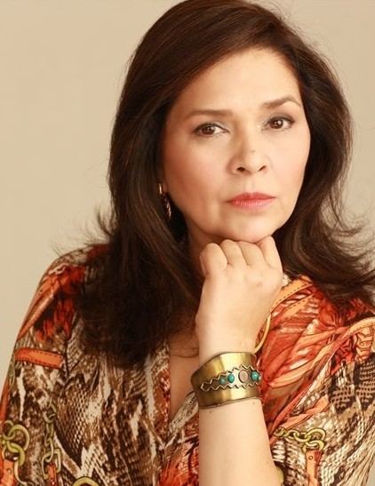 Hilda Koronel posing with her hand in her chin and wearing an orange and brown dress and a gold bracelet in her wrist.