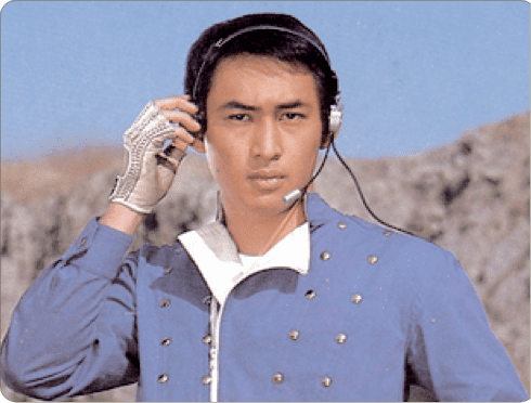 Hiroshi Tsuburaya holding his headphone while wearing silver gloves, and blue long sleeves with gold buttons