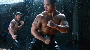 Hiroyuki Ikeuchi as Prince Shiroginomiya, topless while doing a closed fist boxing gesture with a man standing behind him, with tattoos on his body and wearing black pants in a movie scene from The Wrath of Vajra, a 2013 Chinese action film.