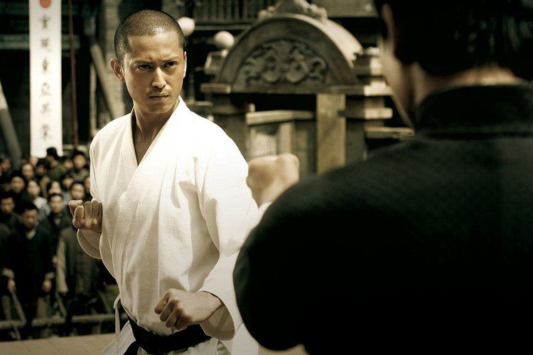 Hiroyuki Ikeuchi as Miura and the back of Donnie Yen. Hiroyuki with a serious face and wearing a white Taekwando uniform in a movie scene from IP Man, a 2008 Hong Kong biographical martial arts film.