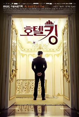 The Cover of the movie Hotel King 2014, Lee Dong Wook standing backward in the middle of a large white and gold plated door, with a chandelier in the center ceiling, hands together at his back, has black hair wearing black coat pants and shoes.