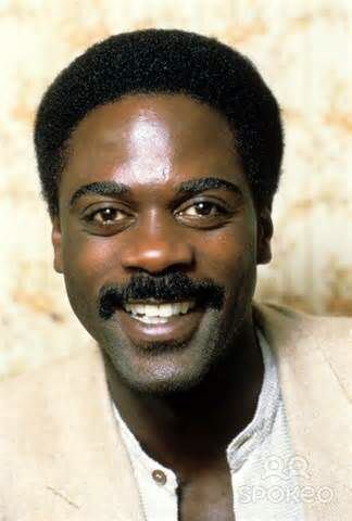 Howard Rollins smiling while wearing cream coat and white long sleeves