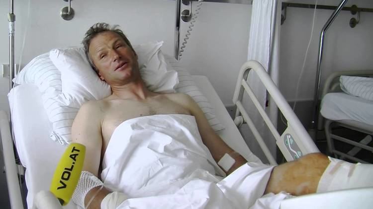 Hubert Strolz lying on a hospital bed with a sad face while topless and covering his body with a white sheet.