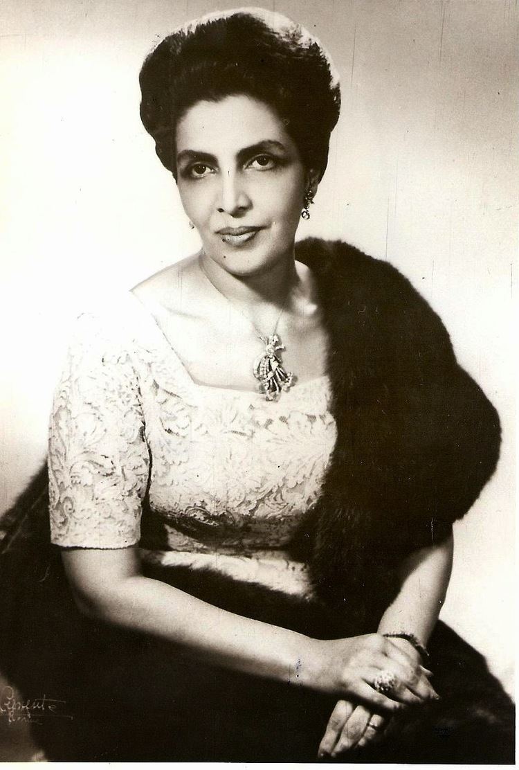 Humaira Begum with a tight-lipped smile while wearing a lace dress, earrings, necklace, ring, and a fur cloth