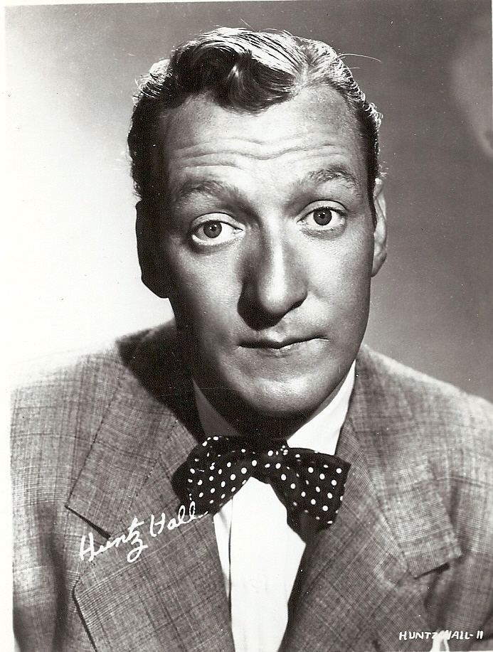 Huntz Hall raising his eyebrows while wearing a gray coat, white long sleeves, and black and white polka dot bow tie
