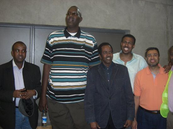 Hussain Bisad looking afar while wearing a striped polo shirt with four men beside him