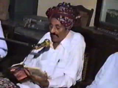 Ibrahim Munshi sitting and talking into a microphone while holding a book