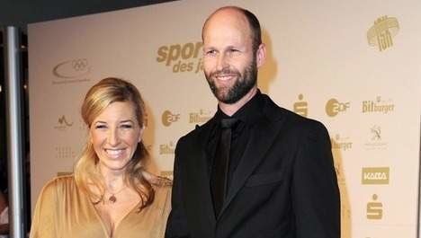 Anni Friesinger-Postma and her husband Ids Postma smiling while attending the red carpet prior to the announcement of the 'German Sports personality of the year' at the Kurhaus in Baden-Baden, Germany. Anni with a blonde half updo hairstyle is wearing a beige blouse while Ids with mustache and beard is wearing a black long sleeve under a black necktie and a black coat