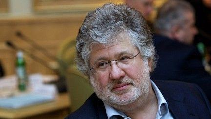 Ihor Kolomoyskyi looking serious with gray hair, white beard, and mustache, wearing a white shirt, a black coat, and eyeglasses