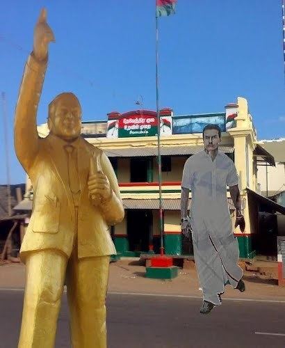 On the left is a statue of Dr. Babasaheb Ambedkar and on the right, An edited image of Immanuvel Devendrar, crossing the road while wearing a white polo, Indian menswear Lungi, and shoes