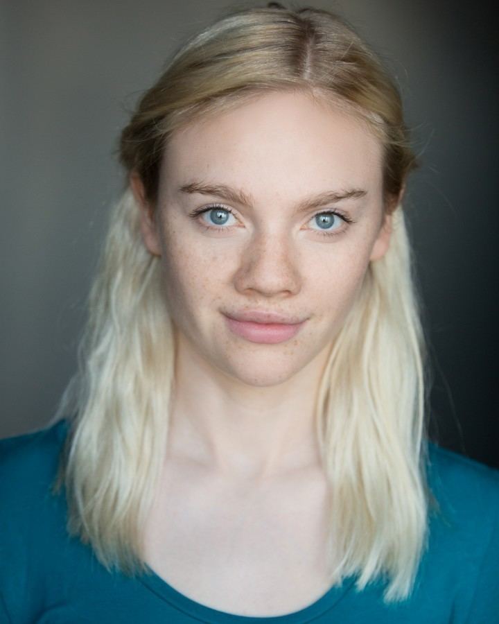Áine Rose Daly smiling with her blonde hair pinned on the sides and wearing a blue blouse