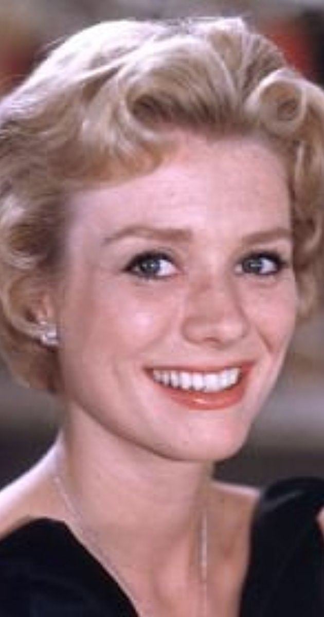Inger Stevens smiling with short curly hair while wearing a black blouse, necklace, and earrings