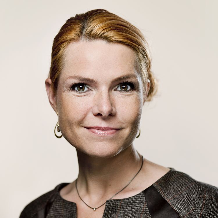 Inger Støjberg smiling and wearing a brown dress and some large earrings.