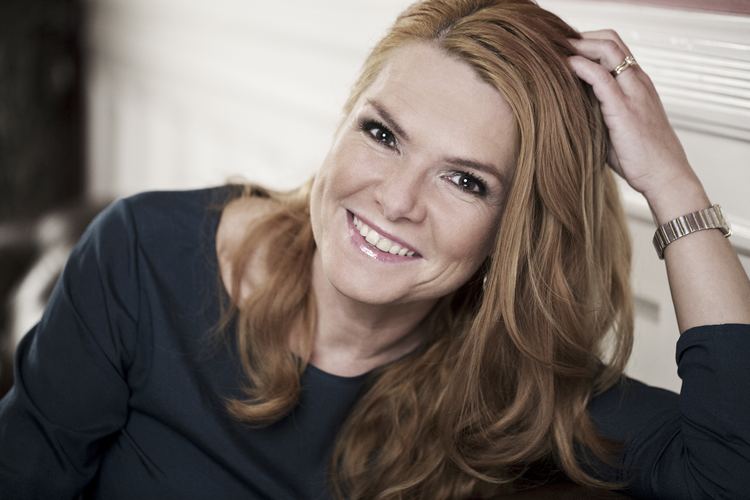 Inger Støjberg smiling with her hand in her hair and wearing a black dress.
