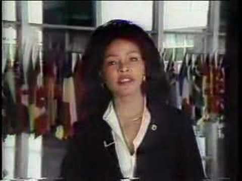 Iola Johnson reporting the news while wearing a black coat, white blouse, necklace, and earrings