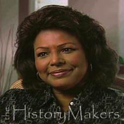 Iola Johnson with a tight-lipped smile while wearing a black and gray blouse and earrings