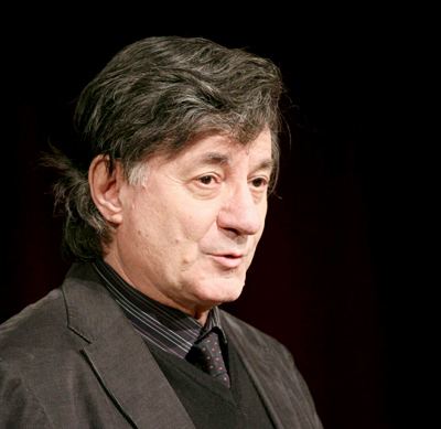 Ion Caramitru wearing a black coat, black vest, black striped long sleeve, and polka dot necktie